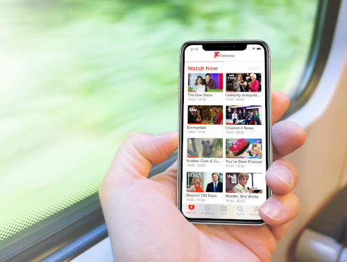 Freeview UK iOS App A man traveling on a train holds a smart phone next to the train window; outside the countryside and rails speed by.
